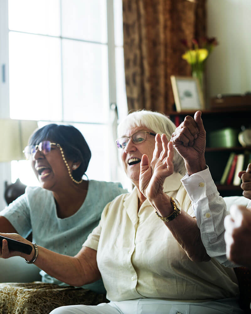 Group of elderly women on the couch watching TV with enthusiastic looks